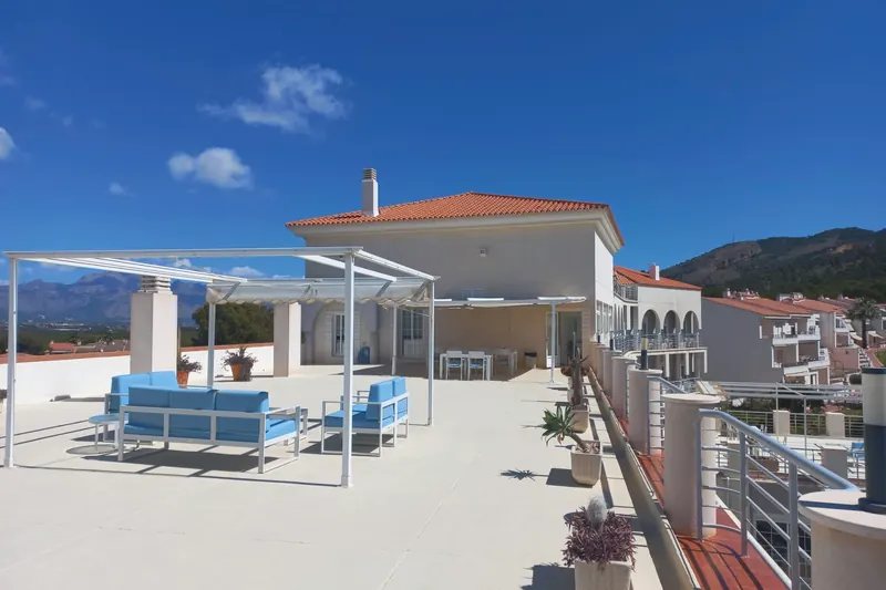 La azotea: una pérgola blanca sobre un sofá y sillones de cojines azules, con la sierra a ambos lados.