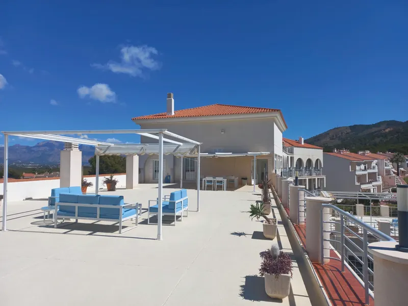 La azotea: una pérgola blanca sobre un sofá y sillones de cojines azules, con la sierra a ambos lados.